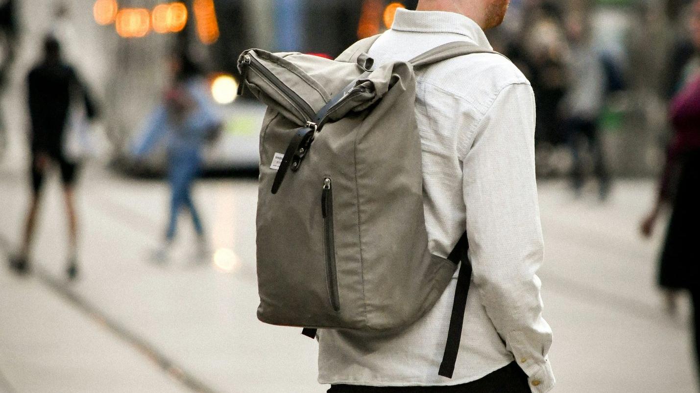 man in white dress shirt and black pants carrying black backpack walking on sidewalk during daytime